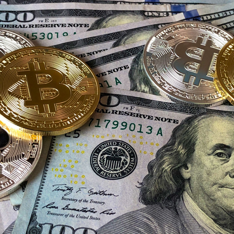 American $100 bills with Bitcoins scattered atop Benjamin Franklin